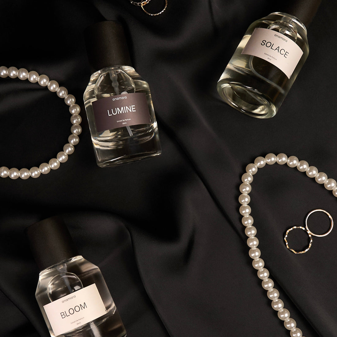 Three perfume bottles labeled 'Lumine', 'Solace', and 'Bloom' on black fabric with jewelry.
